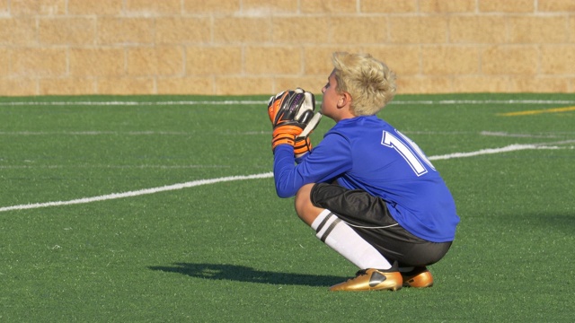 一个男孩在草坪上踢少年足球，当守门员。——慢动作视频素材