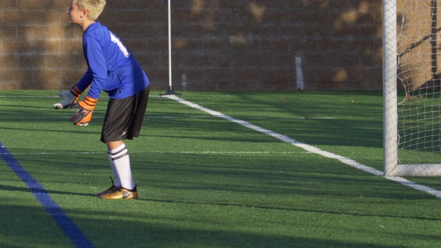 一个男孩在草坪上踢少年足球，当守门员。——慢动作视频素材