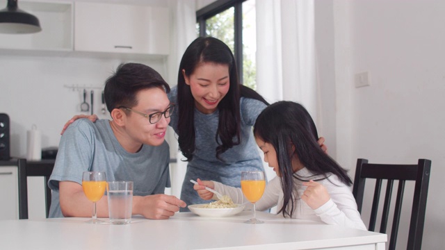 日本亚裔家庭在家里吃早餐。亚洲快乐爸爸，妈妈和女儿吃意大利面喝橙汁在厨房的桌子上早上。视频素材
