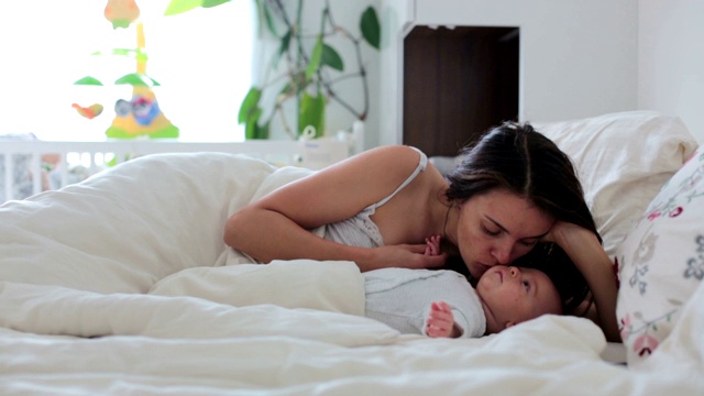 年轻的母亲，抱着她刚出生的儿子在床上，爱抚着他视频素材