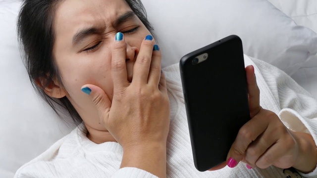 一名亚洲女子躺在床上玩手机后揉眼睛会感到疼痛。手机成瘾的概念。视频素材
