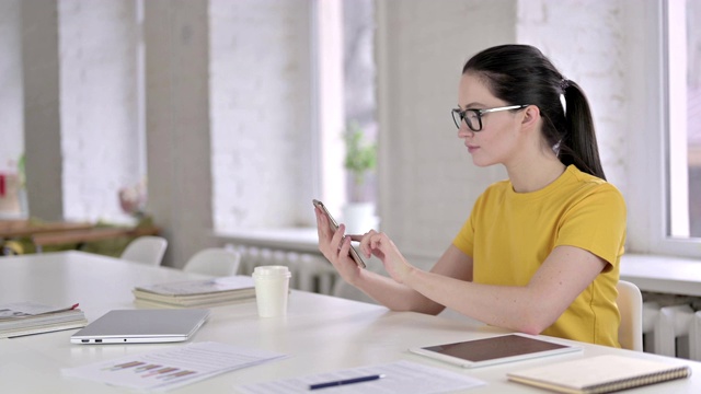 专注于年轻女性设计师在现代办公室中使用智能手机视频素材