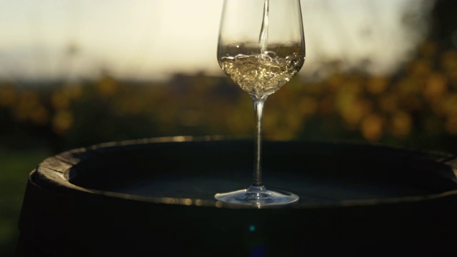 日落时分，将白葡萄酒倒入木桶上的玻璃杯中视频素材