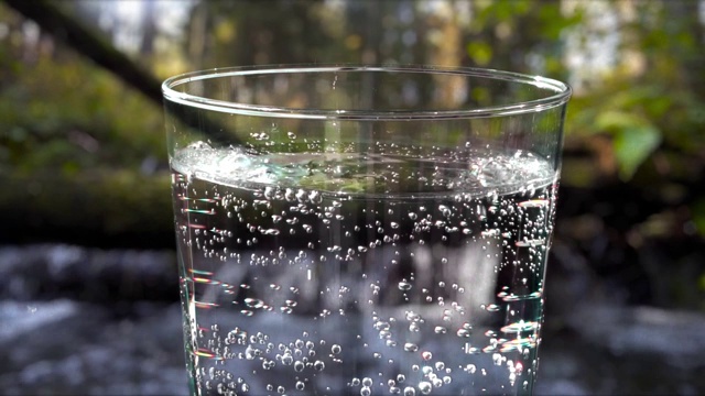 将矿泉水倒进一个以野生景观为背景的玻璃杯中视频下载