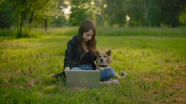 一位漂亮的白人女性在公园里，旁边有一台打开的笔记本电脑，她在抚摸她的狗视频下载
