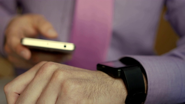 男人正在用他的智能手表和智能手机应用。商人使用时尚的智能手表和智能手机应用程序在触摸屏上。有人在用她的智能手表触摸屏可穿戴设备。视频素材