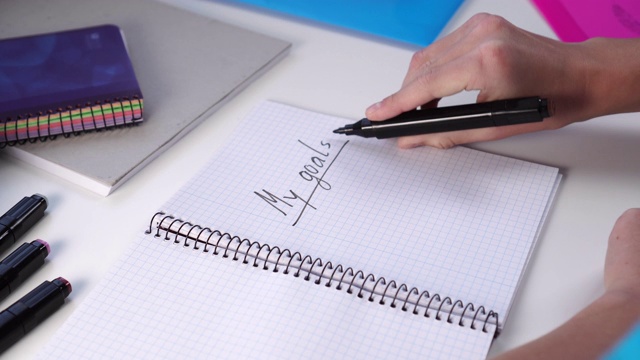 一个青少年用黑色毡尖笔在一张白纸上写下“我的目标”。学生工作场所的笔记本，毡尖笔和塑料文件夹视频下载