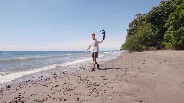 一名白人男性视频博主走在海边沙滩上拍摄自拍视频。视频素材