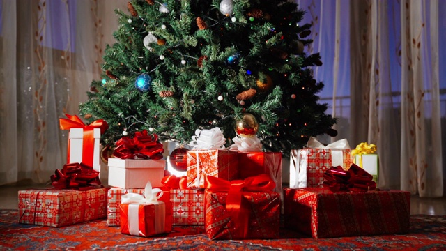 树上闪烁着五颜六色的圣诞花环，树枝上挂着圆圆的塑料球和玩具。冬季装饰和装饰在家里的窗户背景。圣诞树下躺着圣诞礼盒，神奇的冬夜，圣诞庆祝的火花视频素材