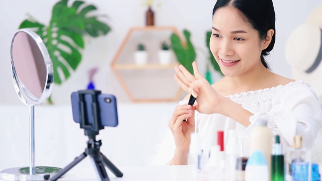 美丽的亚洲女人博客展示如何化妆和使用化妆品。在智能手机前录制视频直播在家。商业在线影响者对社交媒体的概念。视频下载