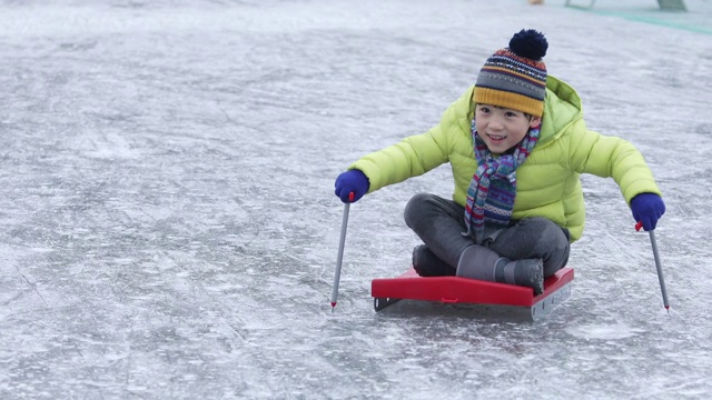 男孩坐在雪橇上滑过冰冻的水库/洪川，韩国视频素材