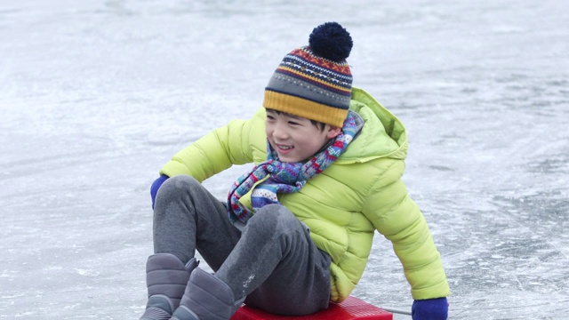 男孩坐在雪橇上滑过冰冻的水库/洪川，韩国视频素材