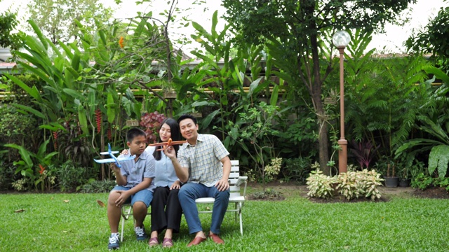 快乐的亚洲家庭母亲，父亲和儿子。他们在家里的花园里一起跑步、玩飞机、模拟。家庭度假。慢动作视频下载
