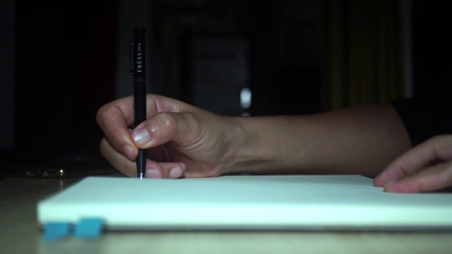 4K视频女人的手写在她的笔记本上，背景是暗室。视频素材