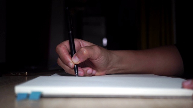 4K视频女人的手写在她的笔记本上，背景是暗室。视频素材