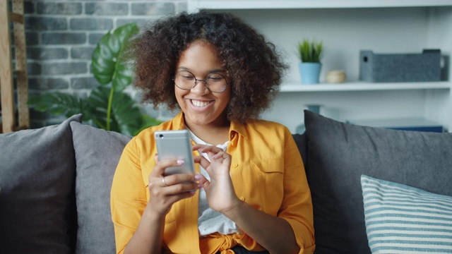 美丽的非洲裔美国女孩使用智能手机在家里笑放松视频素材