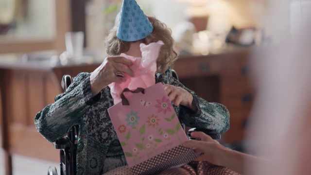 曾孙们看着他们的曾祖母在她的100岁生日聚会上打开一个礼物袋里的生日礼物视频素材
