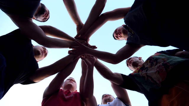 年轻运动员们团结一致地把手一个接一个地叠在一起。一群最好的朋友把他们的手臂放在一个圆圈的中心，并把他们举起到蓝色的天空。友谊和团队合作理念。视频下载