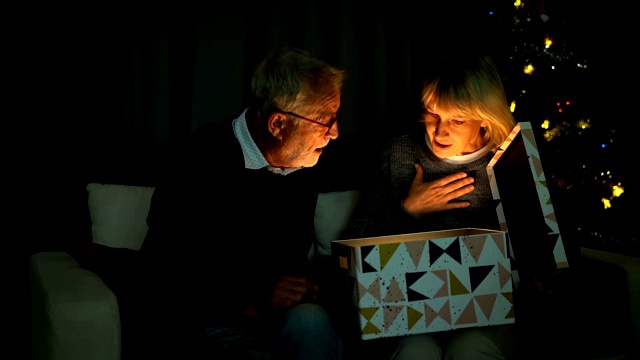 微笑的老年夫妇在圣诞节打开一个装有闪亮爆炸光线的礼盒视频素材