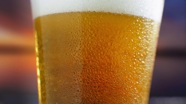 慢镜头宏观冰镇啤酒倒进一个带有汗渍的玻璃杯。啤酒泡沫浮上水面视频素材