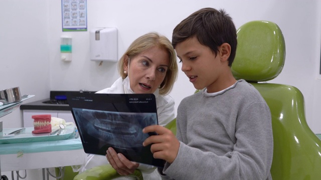 热心的牙科医生一边给年轻的病人看牙齿的x光片，一边向他解释一些事情视频素材