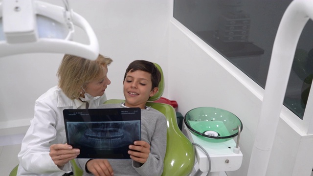 女牙医向躺在牙医椅上看x光片的年轻病人解释视频素材