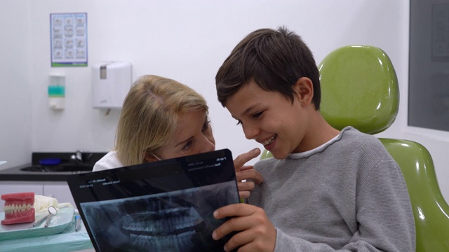 女牙医一边愉快地看着x光片，一边跟年轻的病人解释着什么视频素材