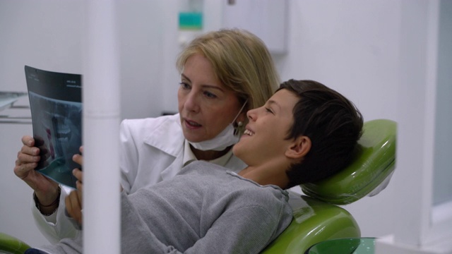 慈爱的女牙医与小儿科病人交谈，给他看他的牙齿的x光，而他躺在牙医的椅子上视频素材