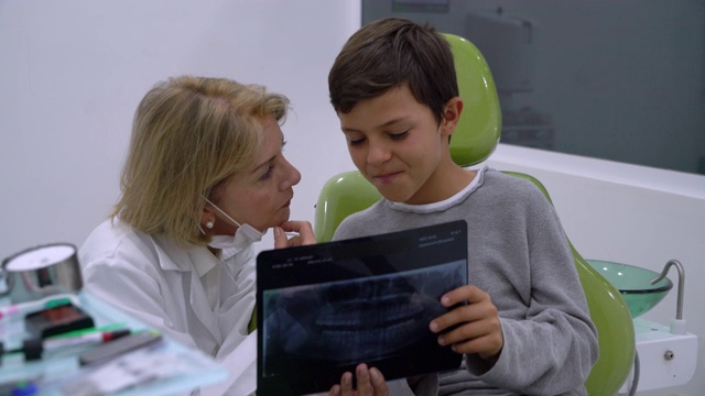 愉快的小男孩看他的牙齿x光，同时向友好的牙医咨询问题视频素材
