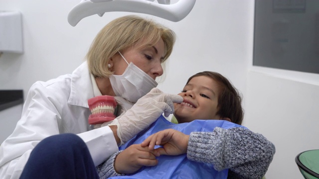 女牙医与小儿科病人交谈，向他展示一个牙齿盒，同时指着他的牙齿在会诊期间视频素材
