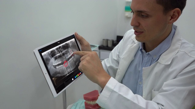 男牙医向病人解释，同时向她展示她的牙齿的x光片，并在平板电脑上圈出不同的牙齿视频下载