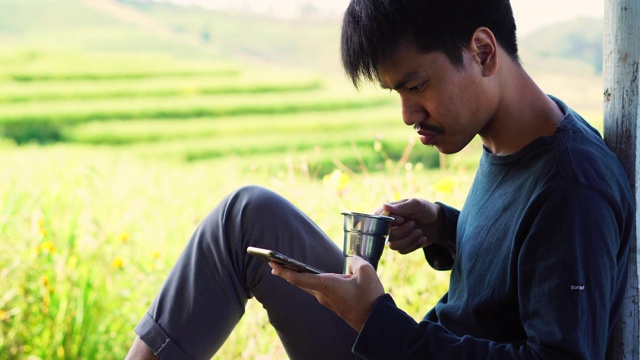一个男人坐在院子里一边喝茶一边用手机视频下载