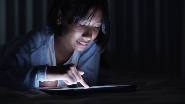 亚洲小女孩晚上在卧室触摸现代数字平板电脑的屏幕。视频素材