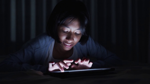亚洲小女孩晚上在床上触摸现代数字平板电脑上的键盘视频素材