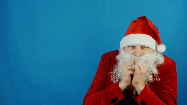 圣诞节和新年，男人像一个圣诞老人在寒冷中颤抖或冻结，在蓝色的背景视频下载