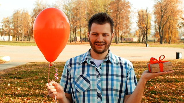 满脸胡须的微笑男子，手里拿着红色气球和礼品盒视频下载