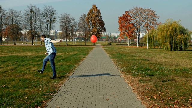 一个穿着衬衫和牛仔裤，带着气球跑的快乐大胡子男人视频素材