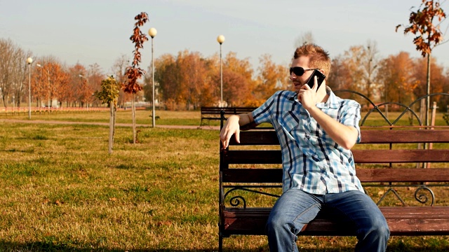 留着胡子、戴着墨镜的时髦男人坐在长凳上打电话视频素材