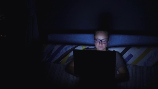 戴眼镜的女人，晚上在窗边用平板电脑喝茶。散景在背景视频下载