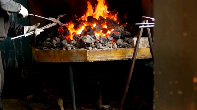 铁匠在熔炉中翻转红热的金属零件，热处理，硬化和加热金属，锻造，慢动作，蹄铁视频素材