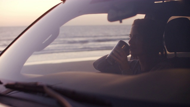 一个年轻女人坐在沙滩上的车里视频素材