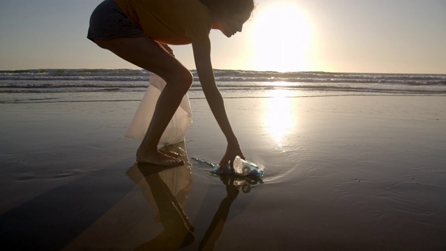 日落时分，年轻女子在海滩上捡垃圾视频下载