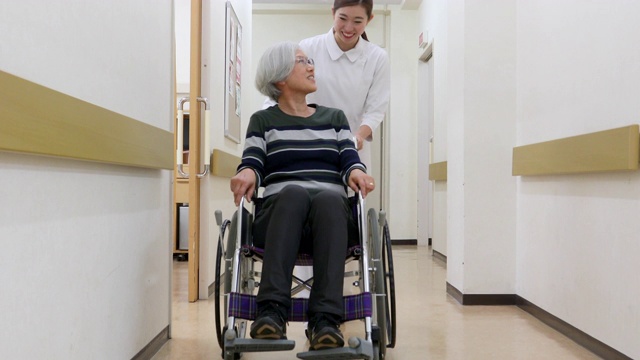 护士推着一位坐轮椅的老年病人穿过医院视频下载