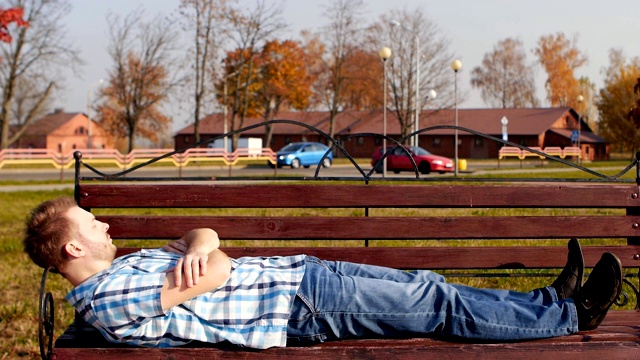 年轻英俊和时尚的白人男子躺在公园的长凳上休息，复印空间，慢动作视频下载