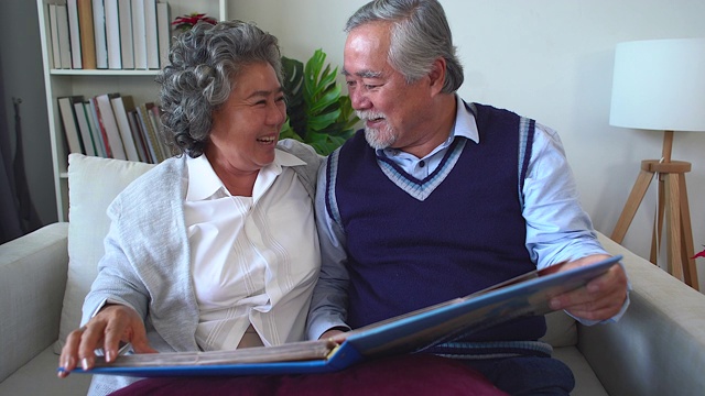 老夫妇打开相册，回忆着快乐的时刻，成年父母在相册里欣赏着回忆青春的照片。退休夫妇花时间看旧相册。视频下载