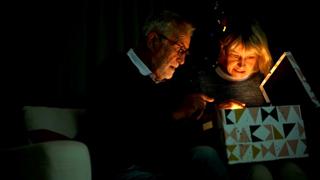 微笑的老夫妇在圣诞节打开一个装有闪亮爆炸光的礼盒的慢镜头视频素材