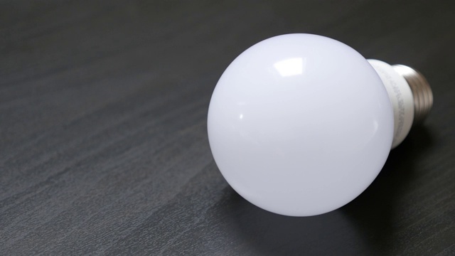 未来的LED灯泡经典灯泡替代木质桌子缓慢倾斜4K视频下载
