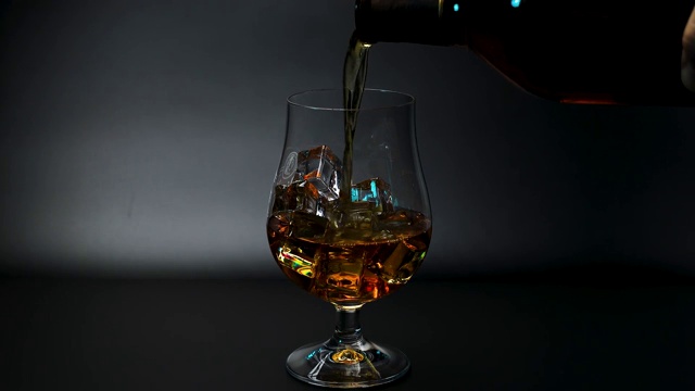 短片显示威士忌被倒入一个郁金香杯与冰在黑色背景。美丽的背景。酒精的概念。视频下载