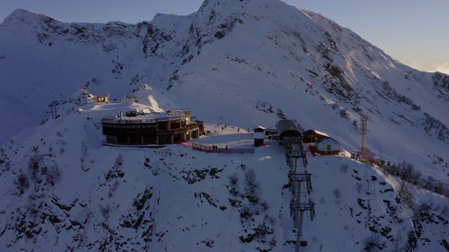 雪山山顶上供滑雪者和滑板者运输的鸟瞰图滑雪缆车站和缆车通道。无人机飞越雪山在冬季滑雪胜地。雪坡上的滑雪电梯视频素材
