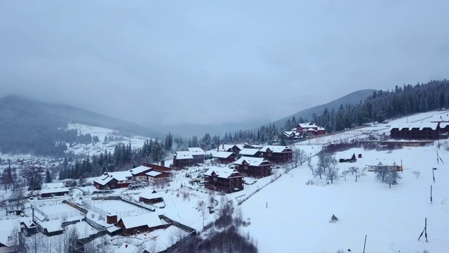 冬季山区有人居住地区的空中航拍。山村的建筑物和房屋在雪坡上覆盖着雪。乡村，冷杉和松树林。滑雪胜地的小屋视频素材
